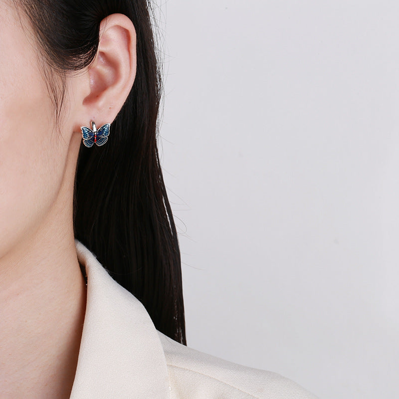 Origsoul butterfly earrings for women in blue worn on ear with white blazer background