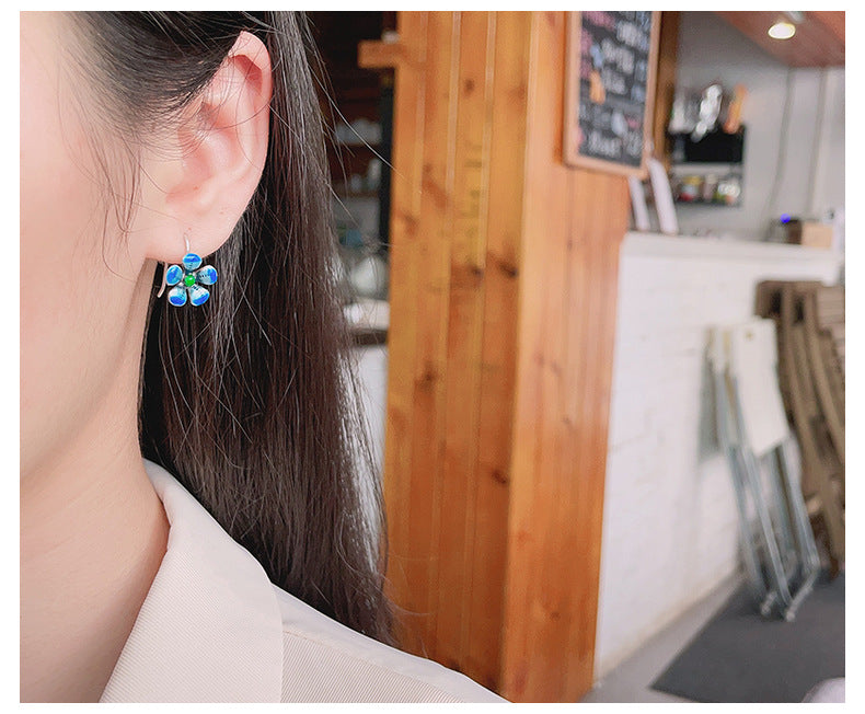 Origsoul daisy tassel earrings worn on ear featuring blue and green floral design in casual indoor setting