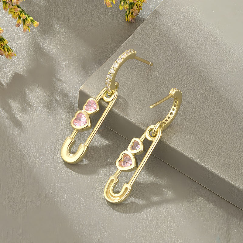 Origsoul gold heart shaped safety pin earrings with pink heart gemstones and hoop detailing