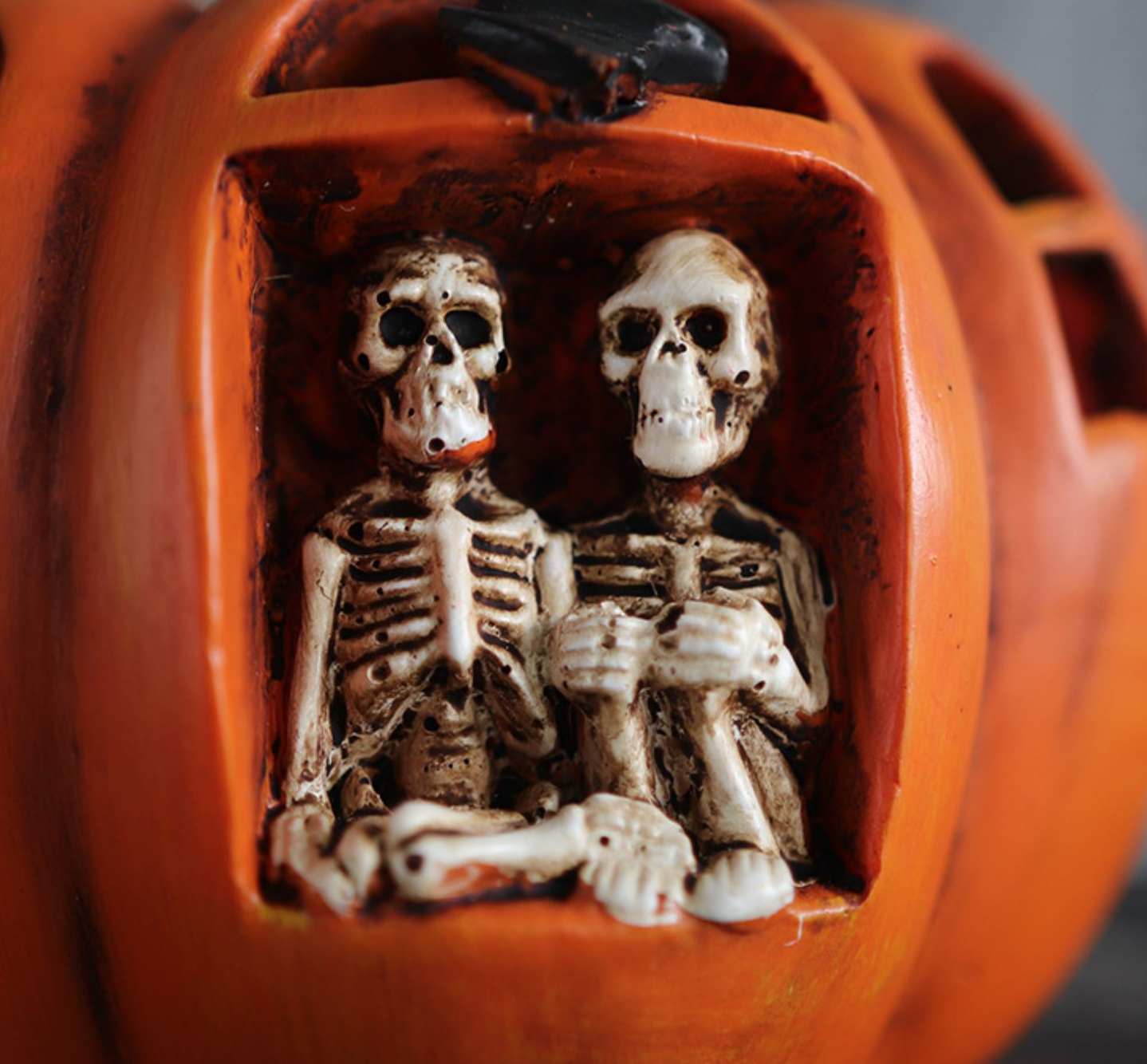Close-up of two skeletons inside an orange resin haunted house pumpkin Halloween decoration
