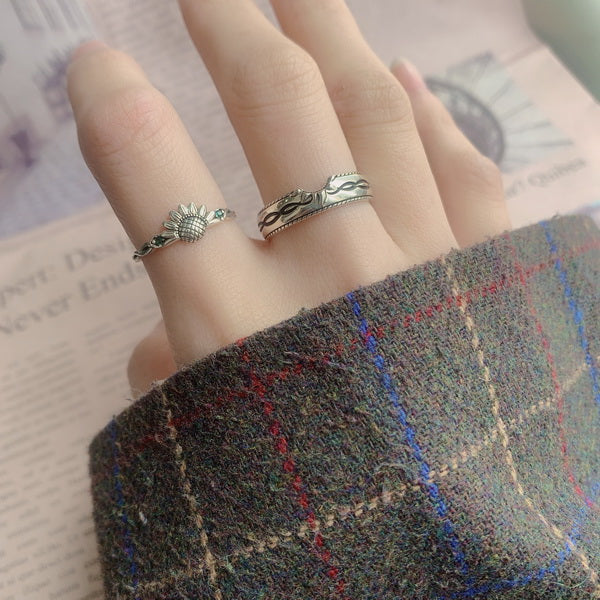 Origsoul sunflower antique ring worn on finger next to a silver patterned band ring with plaid sleeve background