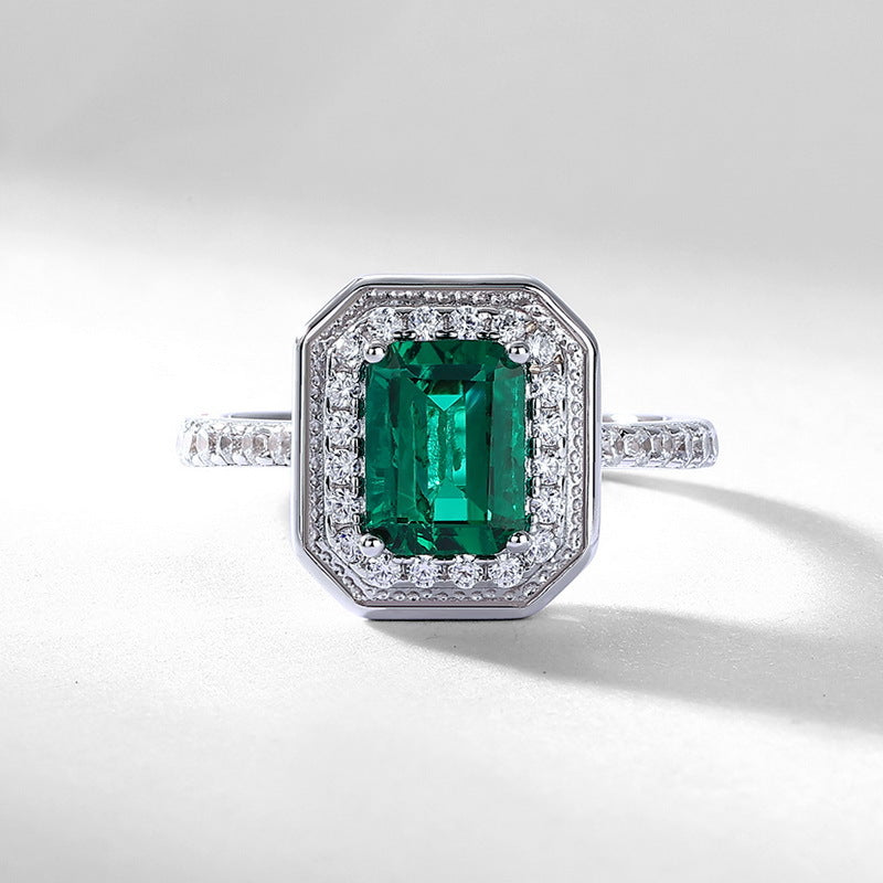 Origsoul emerald cut-engagement ring with a green center stone surrounded by small diamonds on a silver band