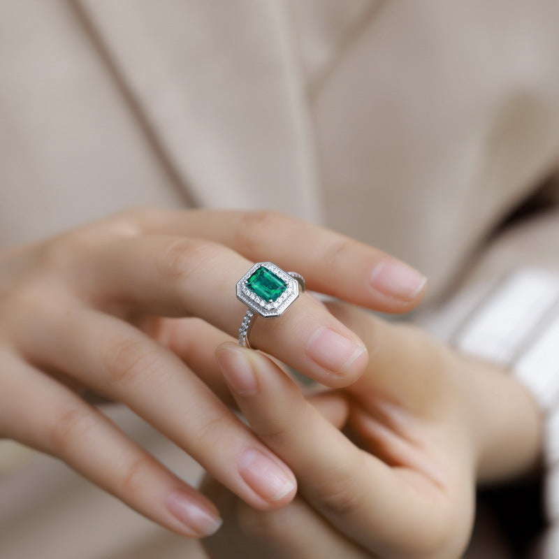 Origsoul emerald cut-engagement ring with a vibrant green gemstone and diamond halo on hand