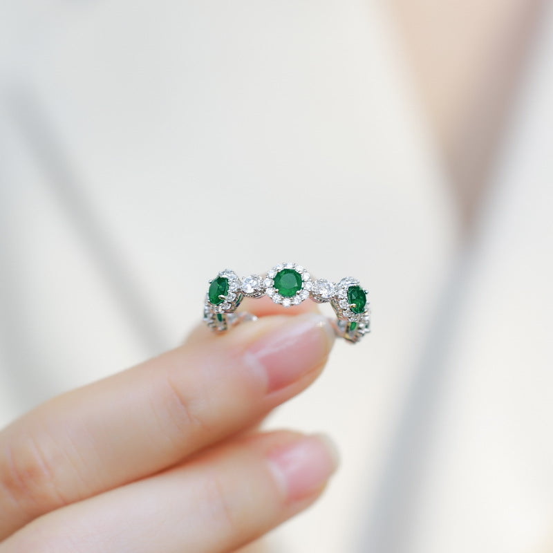 Origsoul engagement ring emerald cut with round green gemstones and diamond accents held between fingers