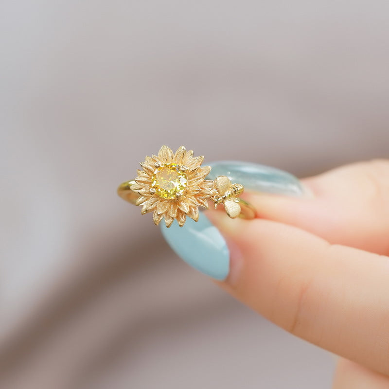 Origsoul silver sterling ring with sunflower design and yellow gemstone held by hand with blue nail polish