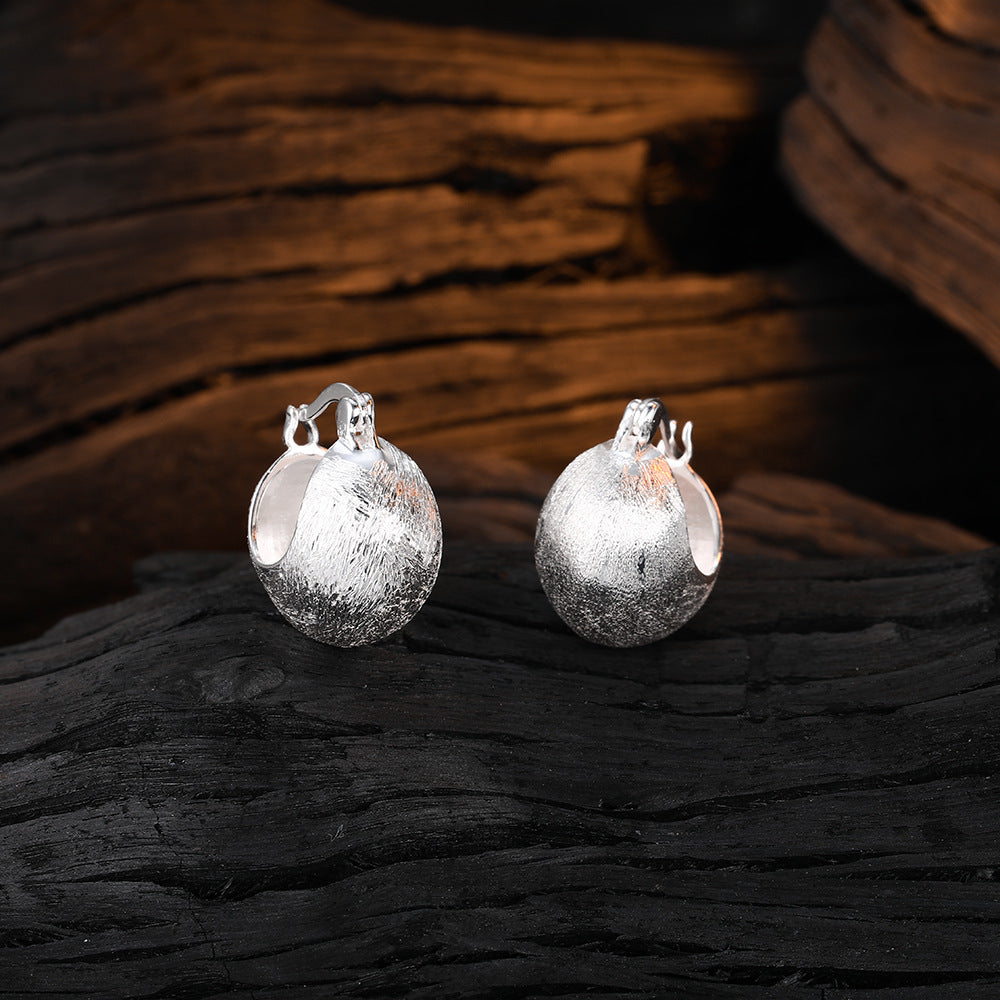 Origsoul hand-drawn silver earrings with textured round design on dark wooden background