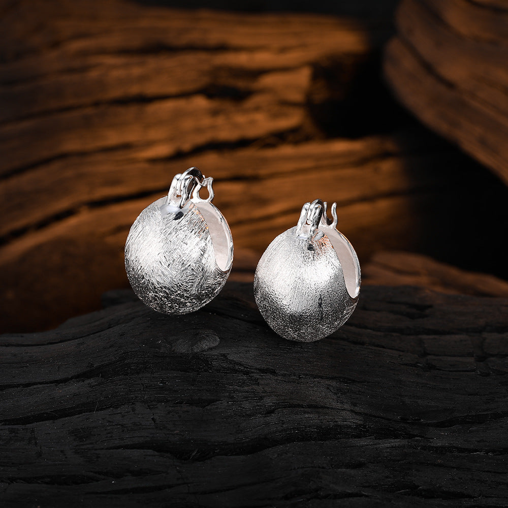 Origsoul hand-drawn silver earrings with textured round design displayed on dark wood background