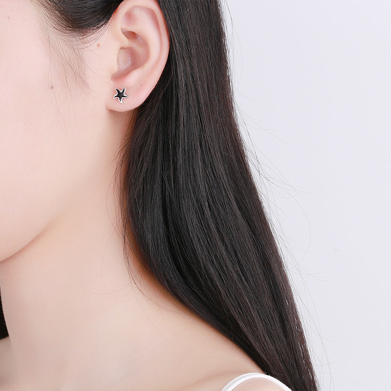 Cosmic jewelry nautical star stud earrings worn on ear with long black hair background