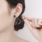 Origsoul retro black enamel earrings with cosmic sun design worn on ear and held in hand