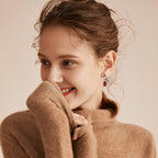 Fashionable rose colored gemstone earrings for women displayed on a smiling model wearing a cozy sweater