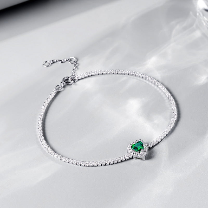 Origsoul bracelet with emerald heart-shaped gemstone and silver chain on reflective surface