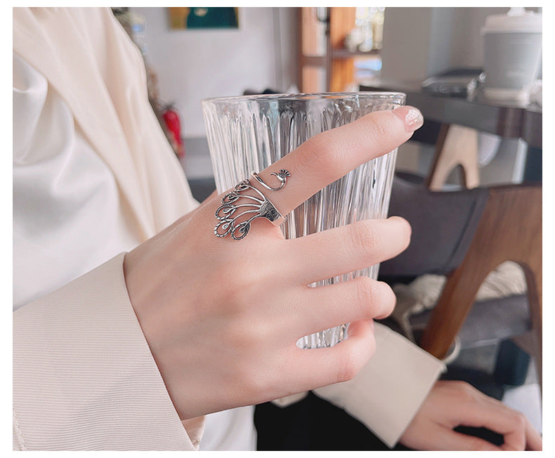 Origsoul peacock adjustable ring for women worn on hand holding a clear glass cup