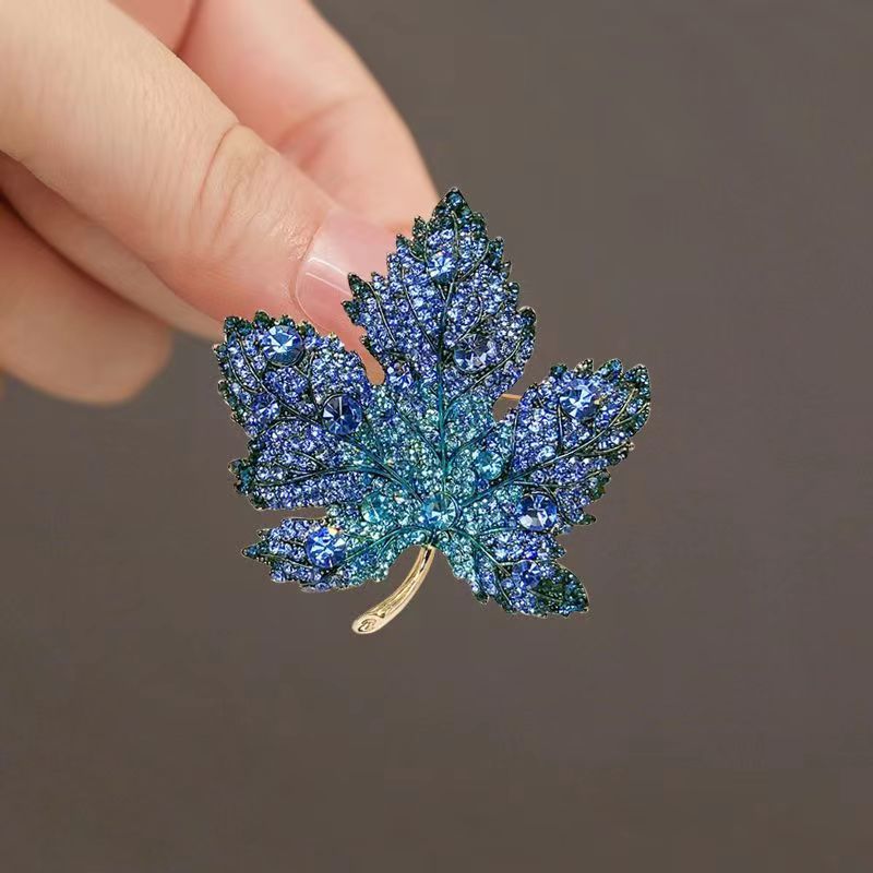 Origsoul blue jeweled brooch shaped like a toronto maple leaf held between fingers